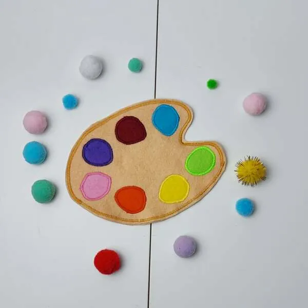 Palette de peinture en feutrine avec pastilles colorées et pompons pour jeu de tri des couleurs.