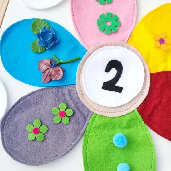 Gros plan fleur en feutrine avec chiffre 2 et éléments à compter sur pétales colorés.