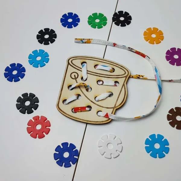 Carte à lacer tambour en bois avec lacet et jetons colorés pour activité de motricité fine enfant.