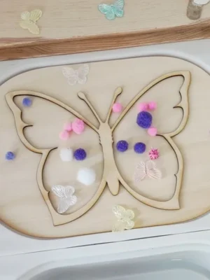 Insert sensoriel papillon en bois pour table d’activité enfant avec pompons colorés.