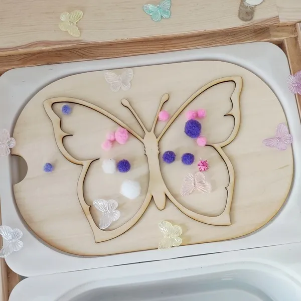 Insert sensoriel papillon en bois pour table d’activité enfant avec pompons colorés.