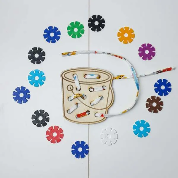 Carte à lacer tambour en bois avec lacet et jetons colorés pour activité de motricité fine.