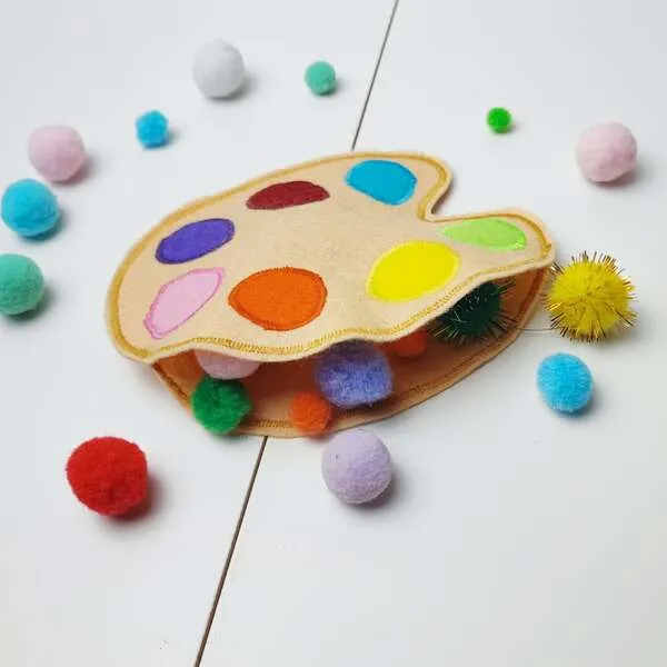 Palette de peinture en feutrine avec pochette remplie de pompons colorés pour activité sensorielle.