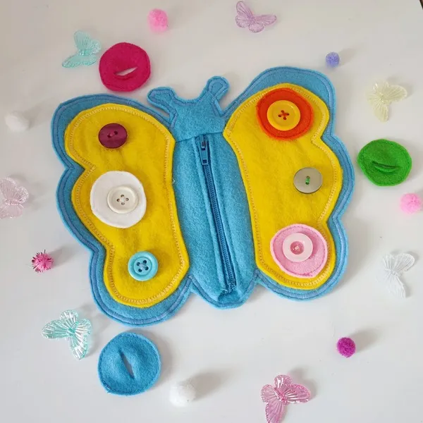 Papillon sensoriel en feutrine avec boutons et fermeture éclair pour activité de motricité fine enfant.