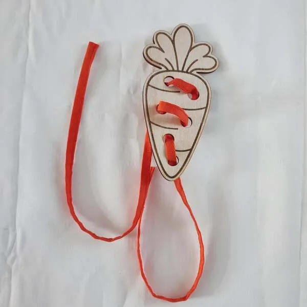 Carte à lacer en bois en forme de carotte avec lacet orange pour activité de motricité fine.
