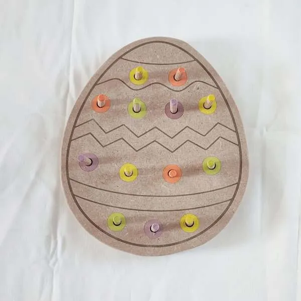 Plateau pic en bois en forme d’œuf de Pâques avec pions colorés pour activité de motricité fine.