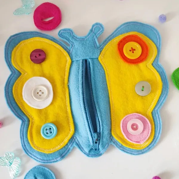 Papillon sensoriel en feutrine avec boutons colorés et fermeture éclair pour activité de motricité fine enfant.