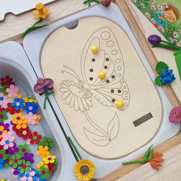 Insert papillon en bois pour table Flisat avec activité de placement de pions et bac rempli de fleurs colorées.