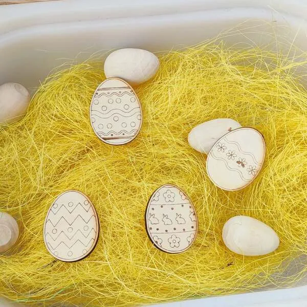 Œufs de Pâques en bois décorés cachés dans un bac sensoriel.