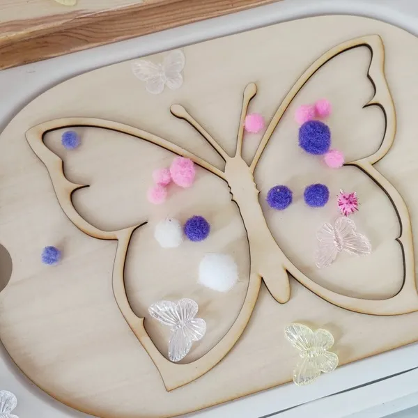 Insert papillon en bois pour table sensorielle enfant avec pompons colorés et papillons décoratifs.