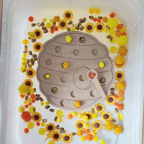 Plateau pompon ruche avec cuillère dans bac sensoriel thème abeille
