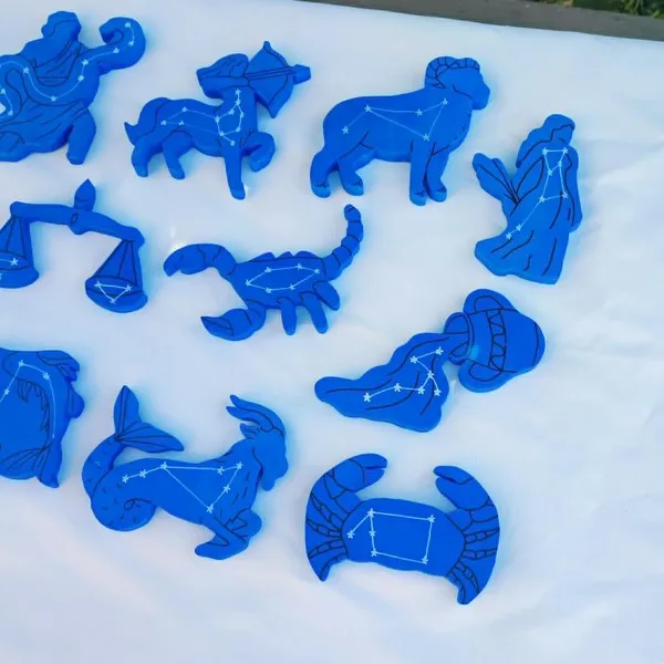 Figurines en bois représentant plusieurs signes astrologiques avec leurs constellations gravées sur fond bleu étoilé.