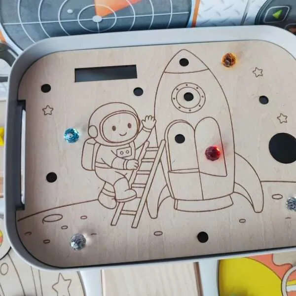 Insert en bois pour bac Livv 2L représentant un astronaute montant dans une fusée avec emplacements à compléter pour travailler la motricité fine.