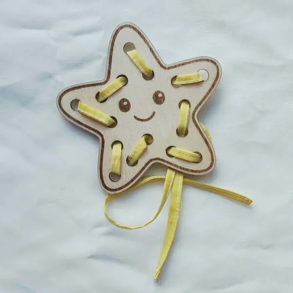 Carte à lacets en bois en forme d'étoile souriante avec ruban jaune à enfiler pour développer la motricité fine.