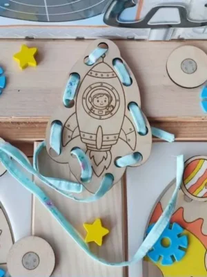 Carte à lacets en bois en forme de fusée avec un astronaute visible dans le hublot et un ruban à enfiler.