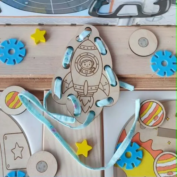 Carte à lacets en bois en forme de fusée avec un astronaute visible dans le hublot et un ruban à enfiler.