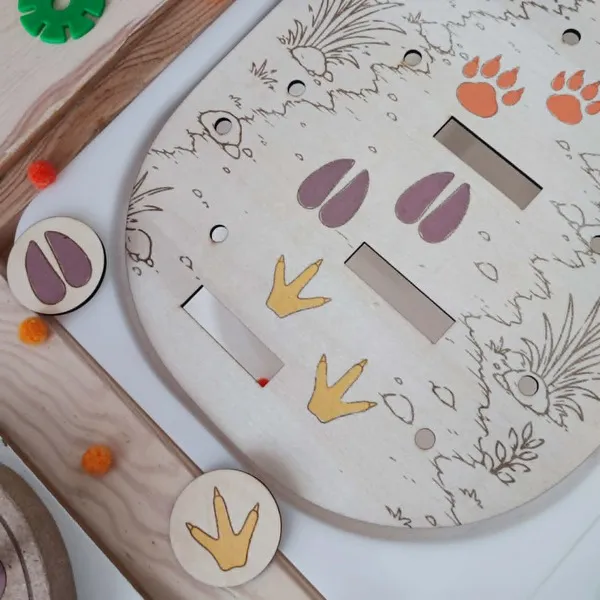 Gros plan sur un plateau éducatif en bois représentant des empreintes d'animaux de la savane. Les enfants associent les jetons illustrant les traces du lion, de la girafe et de l'hippopotame aux bonnes empreintes gravées sur le parcours. Cette activité Montessori développe l'observation, la discrimination visuelle, la logique, la motricité fine et la découverte des animaux sauvages. Idéal pour les assistantes maternelles, MAM, crèches, écoles maternelles et familles.