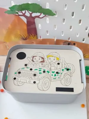 Insert en bois pour bac sensoriel LIVV 2L sur le thème de la savane. Cette activité pédagogique de motricité fine représente deux enfants en voiture de safari. Les enfants utilisent une pince pour placer les pompons dans les différents emplacements du support et développer leur précision, leur coordination œil-main et leur concentration.