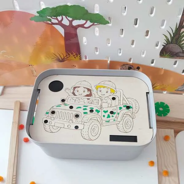 Insert en bois pour bac sensoriel LIVV 2L sur le thème de la savane. Cette activité pédagogique de motricité fine représente deux enfants en voiture de safari. Les enfants utilisent une pince pour placer les pompons dans les différents emplacements du support et développer leur précision, leur coordination œil-main et leur concentration.