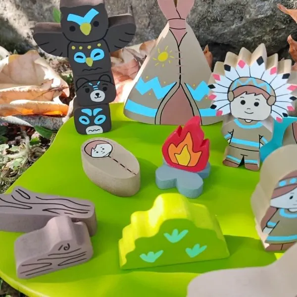 Gros plan sur les accessoires du mini monde en bois des Indiens d'Amérique avec totem, tipi, personnages, bébé emmailloté, feu de camp, rondins de bois et buisson.