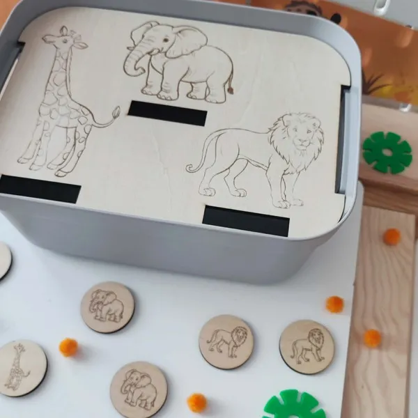 Insert en bois pour bac sensoriel LIVV 2L sur le thème de la savane. Cette activité pédagogique de tri invite l'enfant à associer les jetons représentant un éléphant et un lion aux illustrations gravées sur le support en bois. Un jeu favorisant la motricité fine, la concentration, l'observation et la reconnaissance des animaux de la savane.