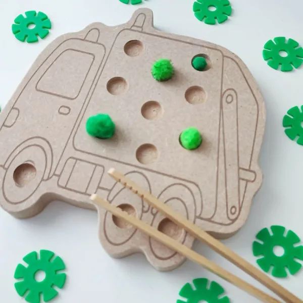 Plateau de motricité en bois en forme de camion poubelle avec des pompons colorés et une pince en bois pour les manipuler.