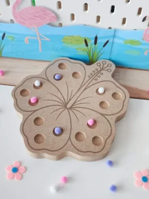 Plateau à pic en forme de fleur d'hibiscus en bois, décoré avec quelques pompons roses, blancs et violets, présenté dans une mise en scène sur le thème du flamant rose.