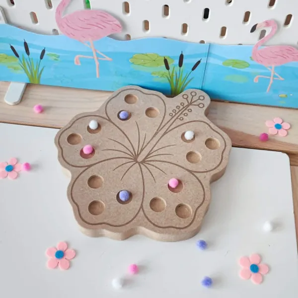 Plateau à pic en forme de fleur d'hibiscus en bois, décoré avec quelques pompons roses, blancs et violets, présenté dans une mise en scène sur le thème du flamant rose.