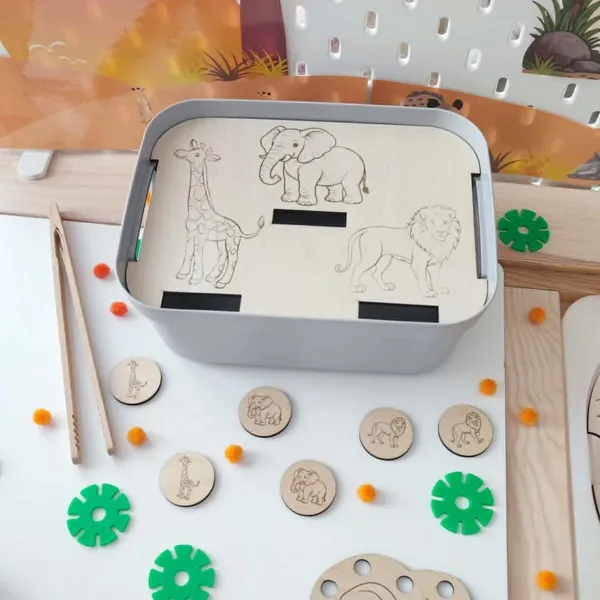 Insert en bois pour bac sensoriel LIVV 2L sur le thème de la savane. Cette activité éducative de tri invite l'enfant à associer les jetons représentant une girafe, un éléphant et un lion avec les illustrations gravées sur le support. Jeu Montessori favorisant la motricité fine, la discrimination visuelle, la concentration et la reconnaissance des animaux sauvages.