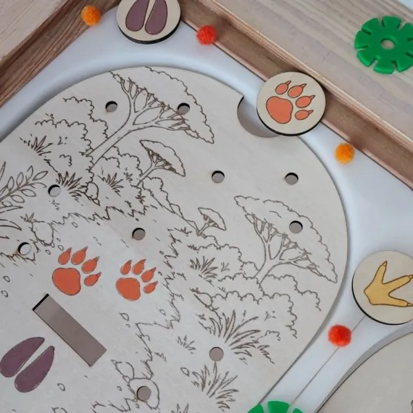 Gros plan sur un plateau éducatif en bois représentant des empreintes d'animaux de la savane. Les enfants observent les traces du lion, de la girafe et de l'hippopotame puis associent les jetons correspondants aux bonnes empreintes. Cette activité Montessori développe l'observation, la discrimination visuelle, la logique, la motricité fine et la découverte des animaux sauvages. Idéal pour les assistantes maternelles, MAM, crèches, écoles maternelles et familles.