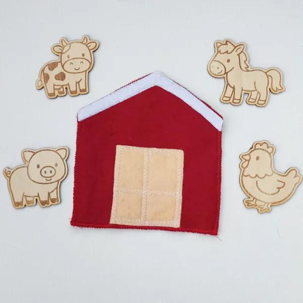 Grange en feutrine rouge accompagnée de quatre figurines en bois représentant une vache, un cheval, un cochon et une poule.