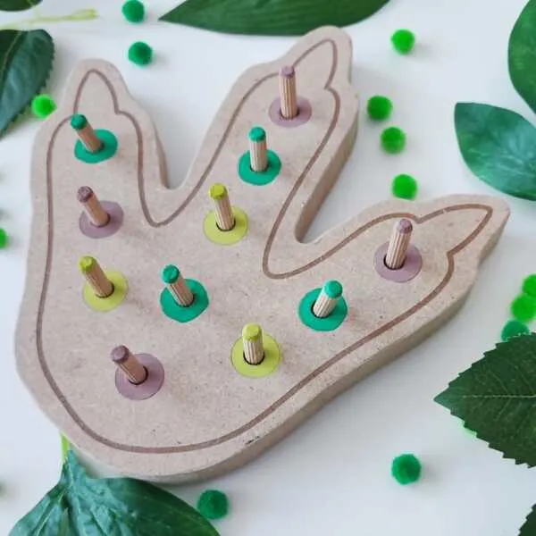 Plateau à pics en bois en forme d'empreinte de dinosaure avec pions et anneaux colorés pour travailler la motricité fine.