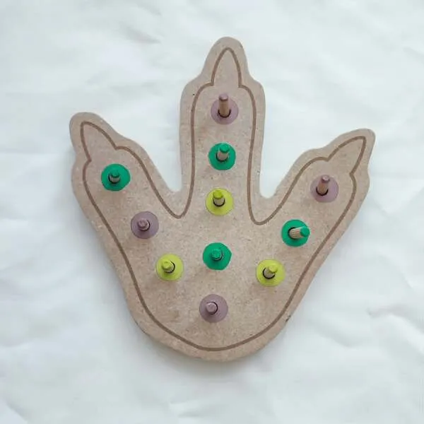 Plateau à pics en bois représentant une empreinte de dinosaure avec des pions colorés pour travailler la motricité fine.