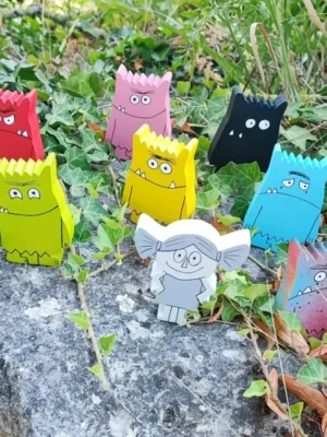 Lot de figurines en bois peintes à la main représentant les monstres des émotions, accompagnées de la petite fille, présentées en extérieur sur un rocher.