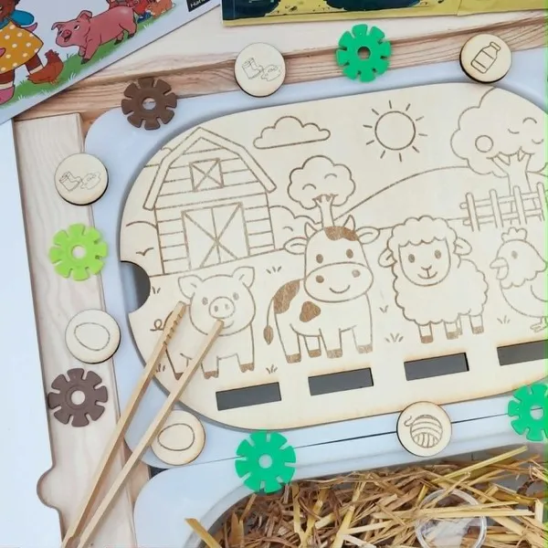 Gros plan sur un insert en bois pour bac Trofast représentant une scène de ferme avec un cochon, une vache, un mouton et une poule. Des jetons illustrés sont à associer aux animaux à l'aide d'une pince.