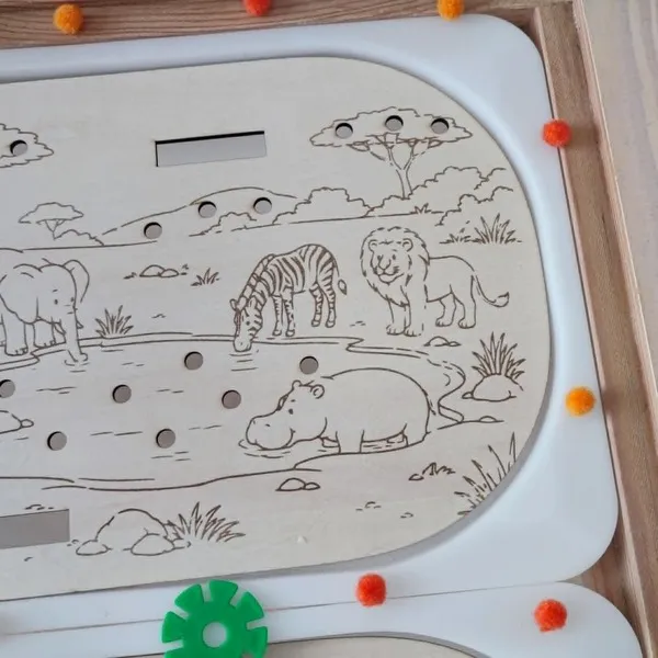 Gros plan d'un plateau éducatif en bois sur le thème de la savane mettant en scène un zèbre, un lion et un hippopotame autour d'un point d'eau. Cette activité Montessori permet aux enfants d'associer les noms des animaux de la savane aux illustrations tout en développant le langage, la reconnaissance visuelle, l'observation et la motricité fine. Idéal pour les assistantes maternelles, MAM, crèches, écoles maternelles et familles.