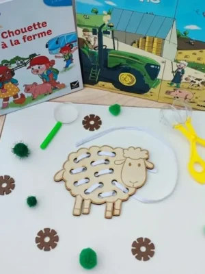 Carte à lacer en bois en forme de mouton avec un lacet blanc permettant de reproduire la toison. Présentée dans un univers sur le thème de la ferme.