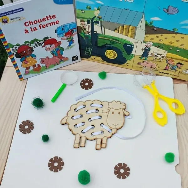 Carte à lacer en bois en forme de mouton avec un lacet blanc permettant de reproduire la toison. Présentée dans un univers sur le thème de la ferme.