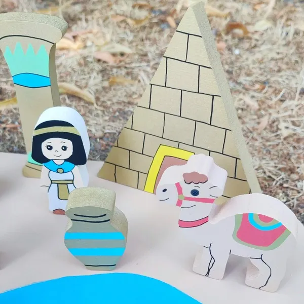 Gros plan sur le mini monde en bois Égypte avec une pyramide, une colonne, une reine égyptienne, un vase décoratif et un chameau peint à la main.