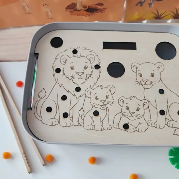 Gros plan sur un insert éducatif en bois pour bac sensoriel LIVV 2L représentant une famille de lions. Le support est conçu pour une activité de motricité fine avec des pompons et une pince. Les nombreux emplacements permettent de compléter le lion, la lionne et les lionceaux tout en développant la coordination œil-main, la précision des gestes et la concentration. Activité Montessori idéale pour les assistantes maternelles, MAM, crèches, écoles maternelles et familles.