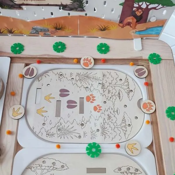 Plateau éducatif en bois sur le thème de la savane avec un jeu de reconnaissance des empreintes d'animaux. Les enfants associent les jetons représentant les empreintes de la girafe, du lion et de l'hippopotame aux traces présentes sur le décor. Cette activité Montessori développe l'observation, la discrimination visuelle, la logique, la motricité fine et la découverte des animaux sauvages. Idéal pour les assistantes maternelles, MAM, crèches, écoles maternelles et familles.