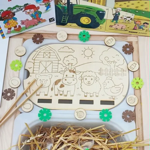 Insert en bois pour bac Trofast représentant une scène de ferme avec un cochon, une vache, un mouton et une poule. Des jetons illustrés sont à associer aux animaux. Le support est présenté dans un bac sensoriel avec de la paille.