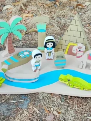 Mini monde en bois sur le thème de l'Égypte avec pyramide, palmier, colonne, barque, personnages, chameau, crocodile et rivière, présenté en extérieur.