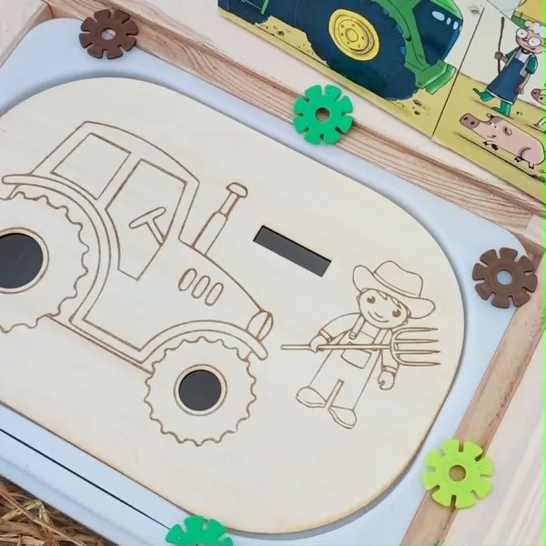 Gros plan sur un insert Trofast en bois représentant un tracteur et un fermier, conçu pour une activité de motricité fine avec des jetons à insérer. Le support est présenté dans un univers inspiré de la ferme.