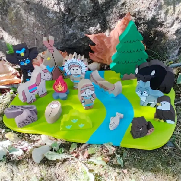 Mini monde en bois sur le thème des Indiens d'Amérique avec personnages, animaux, tipi, canoë, feu de camp et rivière, présenté en extérieur dans un décor naturel.