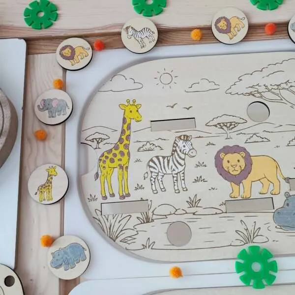Gros plan sur un plateau d'activité en bois représentant les animaux de la savane. Les enfants associent des jetons illustrés (lion, girafe, zèbre, éléphant et hippopotame) aux animaux présents sur le décor. Ce jeu éducatif favorise l'observation, la reconnaissance visuelle, le vocabulaire, la motricité fine et l'autonomie. Activité Montessori idéale pour la maternelle, les assistantes maternelles, les MAM, les crèches et les écoles.