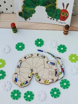 Carte à lacer en bois représentant une chenille, avec un lacet coloré à enfiler et des jetons verts et blancs, inspirée de La chenille qui fait des trous.