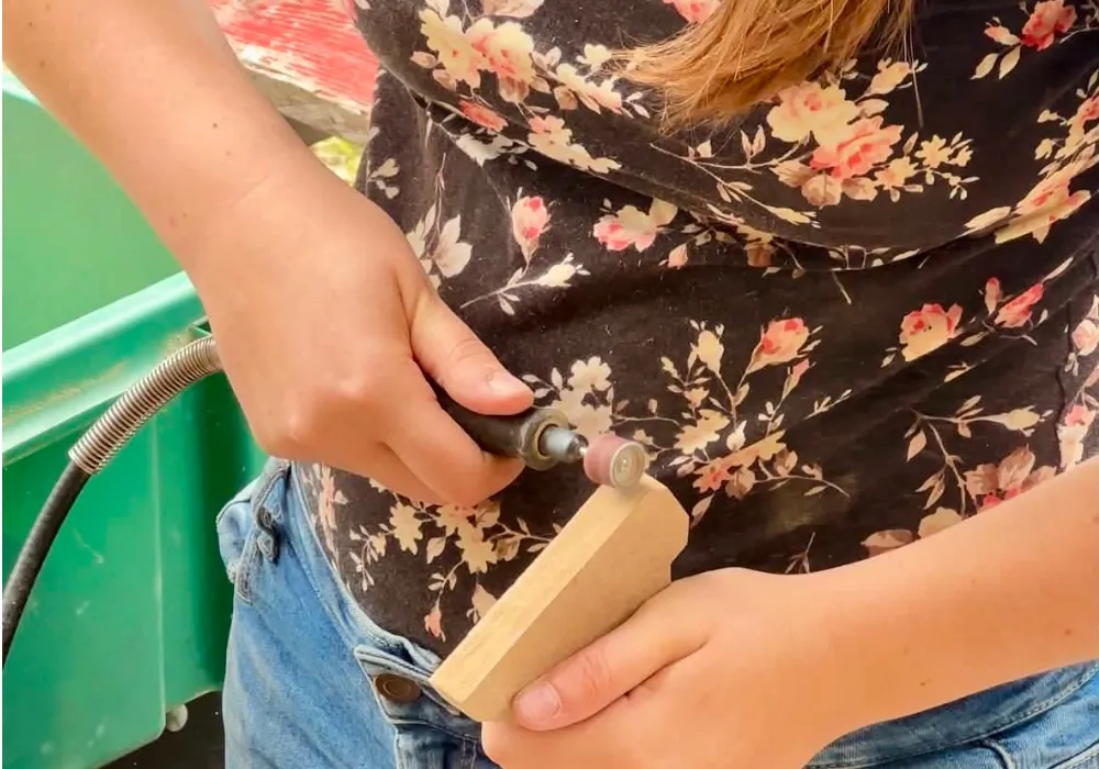 Ponçage manuel d'une création en bois avec un outil rotatif dans l'atelier de fabrication.<br />
