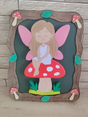 Cadre décoratif en bois avec fée aux ailes roses assise sur un champignon rouge