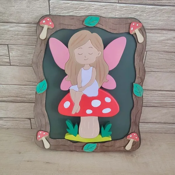 Cadre décoratif en bois avec fée aux ailes roses assise sur un champignon rouge